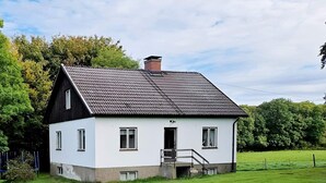 Una casa bianca a due piani con tetto scuro, un piccolo portico e una porta ben visibile.