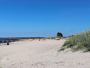 A sandy beach with a pier extending into the water, surrounded by dunes and sparse vegetation. - 9 Person Holiday Home in Bastad (Bastad)