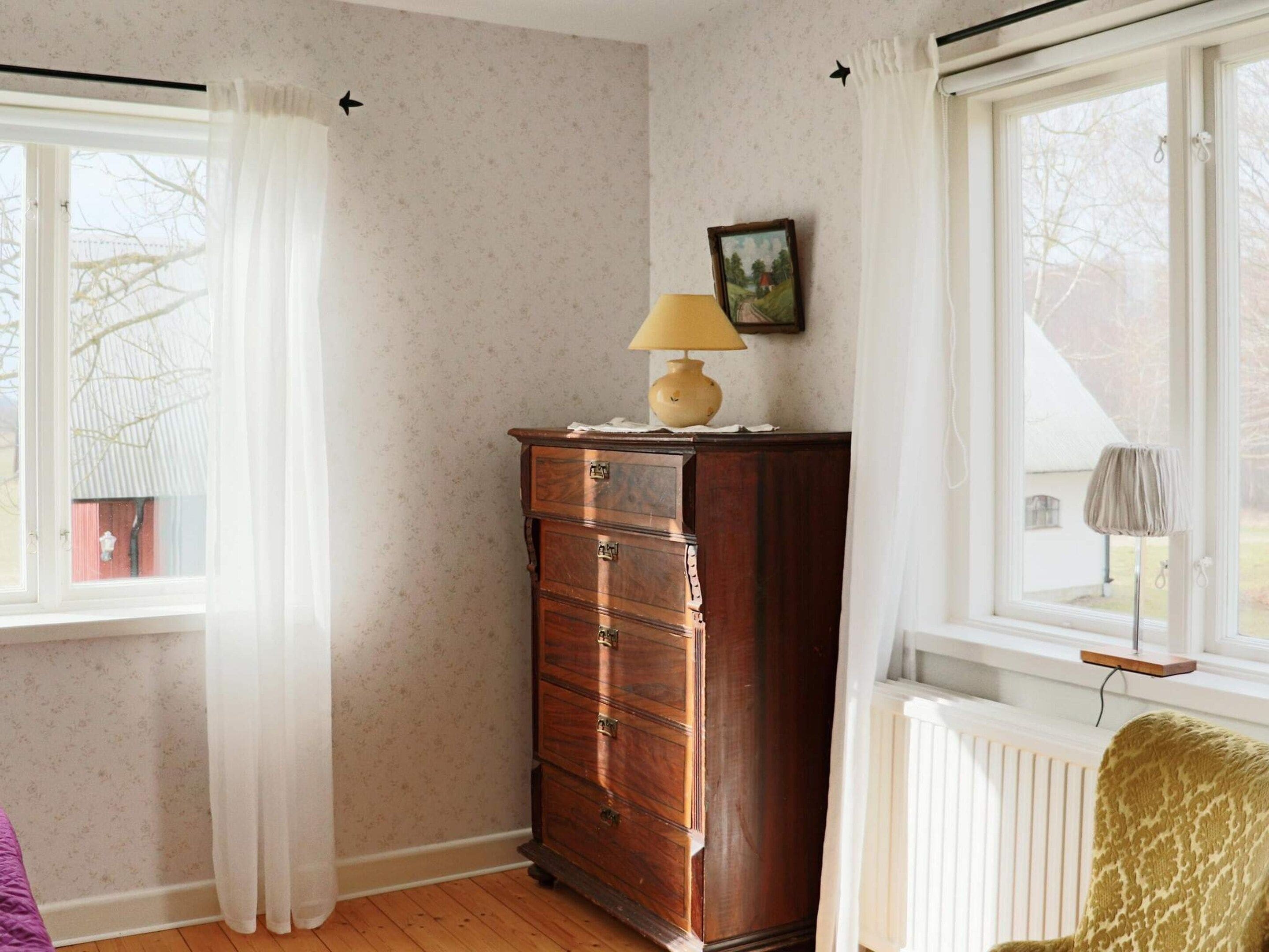 A room with a wooden dresser, a lamp, and a window with curtains.