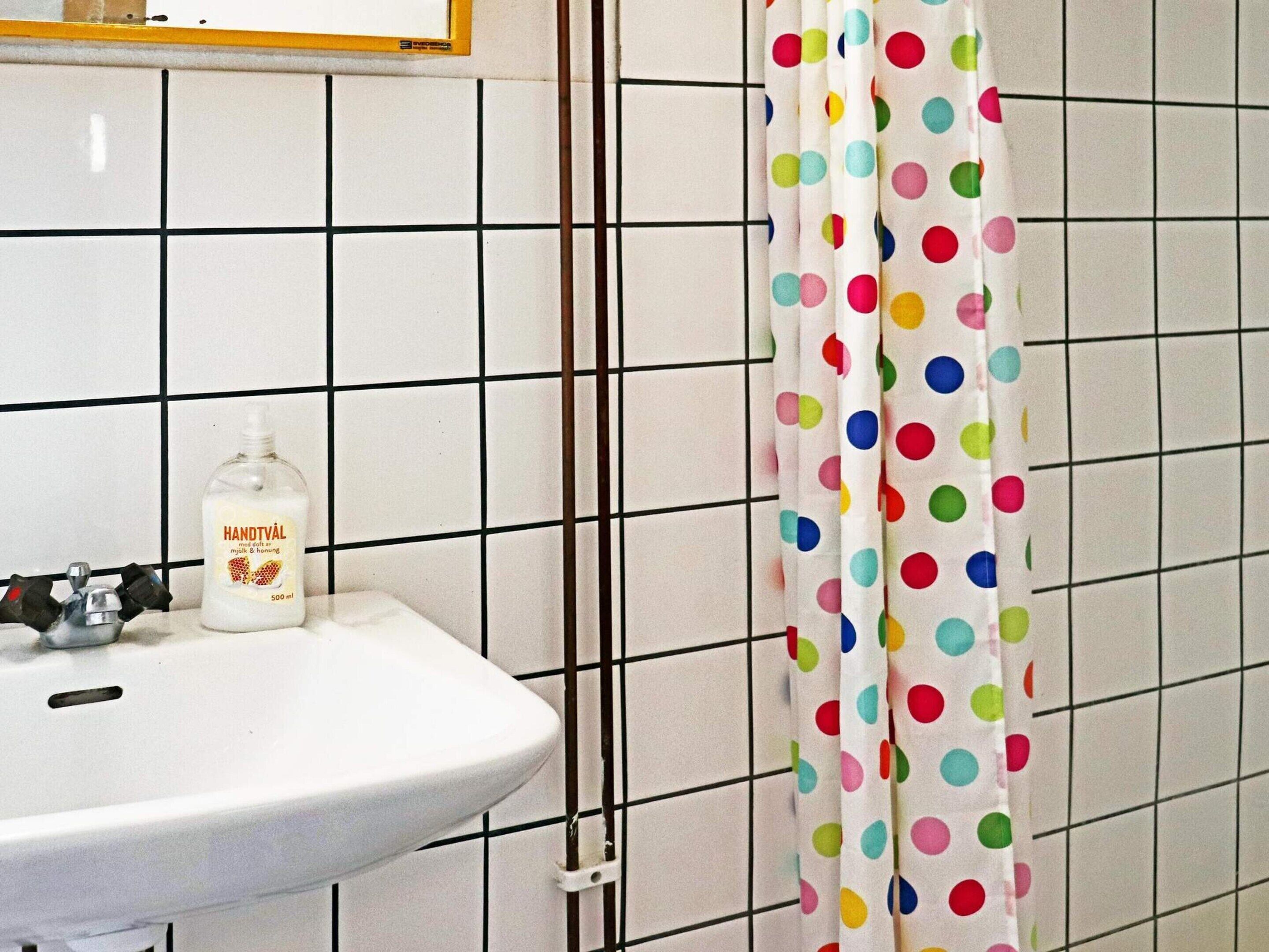 A bathroom with a white sink, a bottle of hand soap, and a polka-dotted shower curtain.