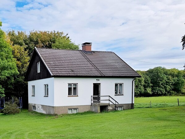 Een wit huis met twee verdiepingen, een donker dak, een klein portaaltje en een duidelijke deur.