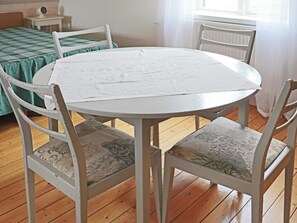 A round white table with four chairs, each with a patterned cushion, in a room with wooden flooring and a bed with a green checkered bedspread. - 9 Person Holiday Home in Bastad (Bastad)