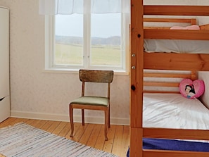 Une chambre avec un lit superposé, une chaise, une fenêtre donnant sur la campagne et un tapis à motifs.