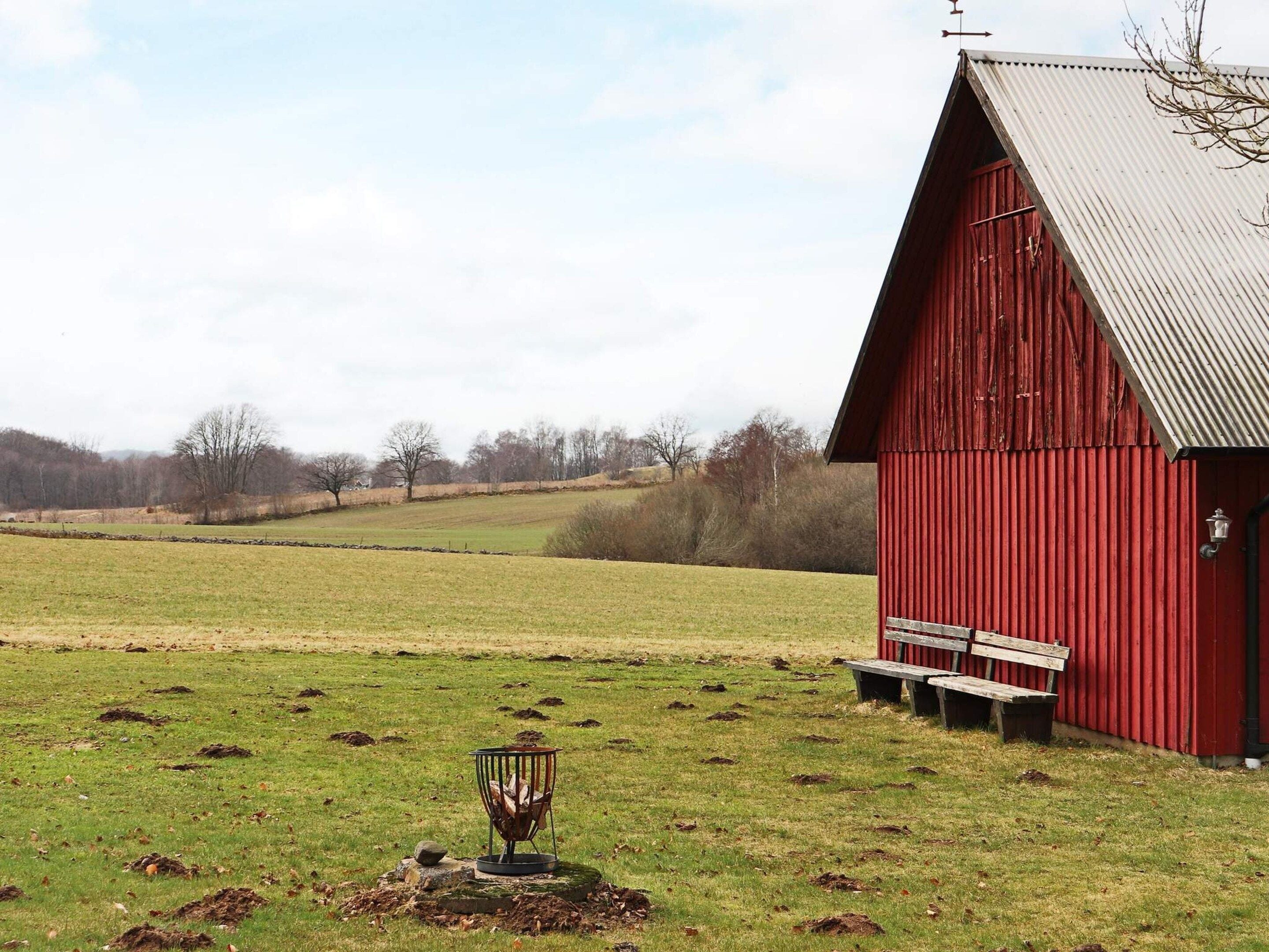A red barn with a sloped roof, a bench, and a bird feeder in a grassy field.
