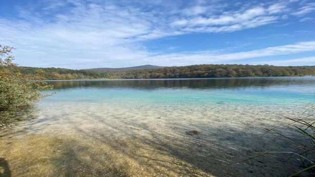 Un lago transparente con fondo visible y bosque circundante.