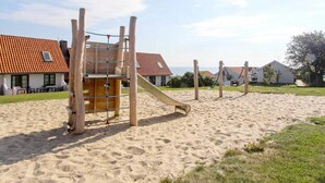 Un parque infantil con arena, una estructura de madera para escalar y un tobogán.