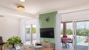 Un coin repas avec une table dressée pour deux personnes, un téléviseur fixé au mur et une vue sur une piscine, visible à travers des portes vitrées.