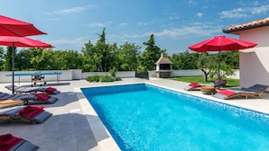 A swimming pool with lounge chairs and red umbrellas, surrounded by greenery and a clear sky. - Villa Lena Comfortable Holiday Residence (Marcana)