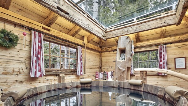 Una cabaña de madera con un jacuzzi grande de madera, paredes de madera y un tragaluz.