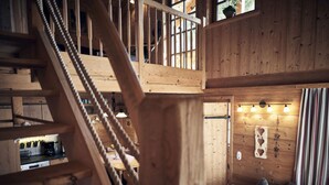 Un interior de madera con una escalera, un área de comedor con una mesa dispuesta para cuatro personas y una pared con un accesorio de luz decorativo.