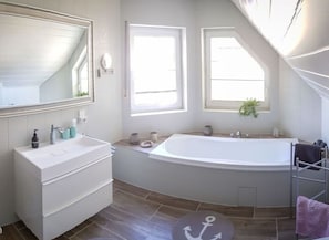 A modern bathroom with a freestanding bathtub, a vanity with a mirror, and two windows providing natural light. - Holiday Apartment in the Tower (Oberfell)
