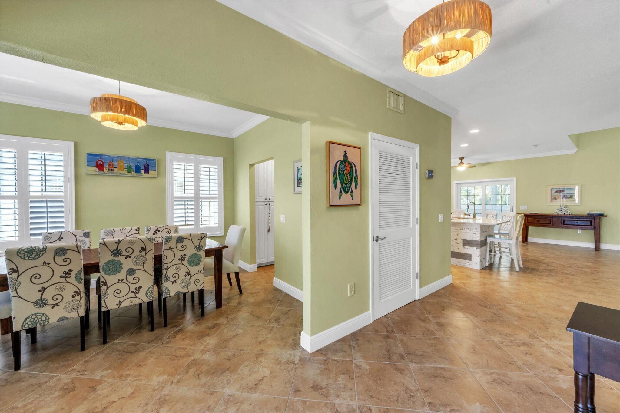 A spacious dining area with a long table and chairs, a door with a decorative panel, and a ceiling fan.