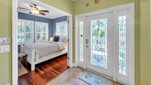 A bedroom with a bed, a ceiling fan, and a view through a glass door. - Cheeky Chateau – 4BR Pool Home in Holmes Beach, Anna Maria Island, FL (Holmes Beach)