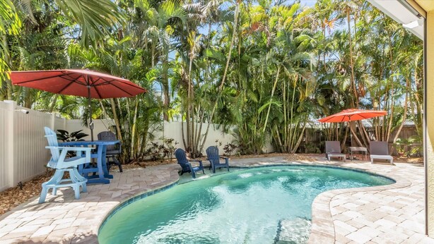 A backyard with a swimming pool, patio furniture, and tropical plants. - Cheeky Chateau – 4BR Pool Home in Holmes Beach, Anna Maria Island, FL (Holmes Beach)