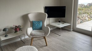 A modern living room with a plush armchair, a flat-screen TV, and a small side table. - Klaar Kimming Modern Retreat (Sylt)