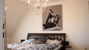 A bedroom with a large bed, a chandelier, a statue, and a bedside table. - Holiday Apartment Zirbelnuss (Augsburg)