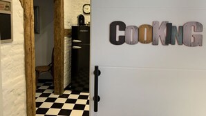 A kitchen area with a black refrigerator, a clock on the wall, and a sign that reads "Cooking". - Cathedral Whispers Modern Retreat (Schwerin)