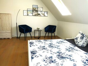 Une chambre à coucher comprenant un lit, deux chaises, une petite table et un mur orné de tableaux.