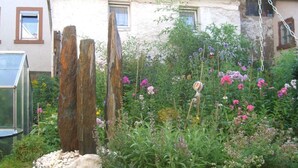 A garden with a variety of plants and flowers, a wooden structure, and a house with a tiled roof in the background. - Apartment in Tauberbischofsheim (Tauberbischofsheim)