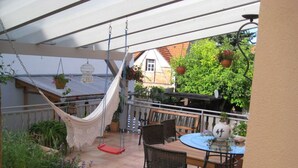 A covered patio with a hammock, wicker chairs, a round table, and potted plants. - Apartment in Tauberbischofsheim (Tauberbischofsheim)