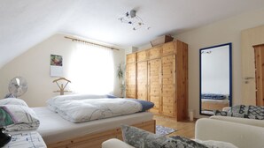 A bedroom with a bed, a wooden wardrobe, a mirror, and a window with curtains. - Apartment in Tauberbischofsheim (Tauberbischofsheim)