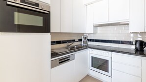 A modern kitchen with white cabinets, a stainless steel oven, a dishwasher, and a coffee maker.