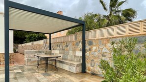 Un patio couvert avec un mur en pierre, un banc et une table.