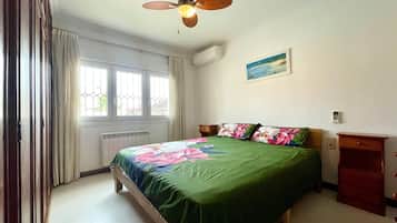 A bedroom with a bed, a ceiling fan, a window, a radiator, and a nightstand.