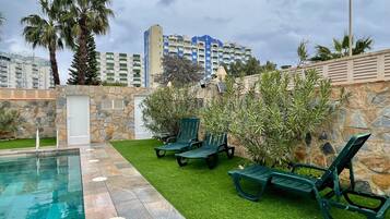 Relax by the pool surrounded by lush greenery and a stone wall.