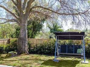 Relax in a serene backyard oasis with a shaded seating area and a majestic tree.