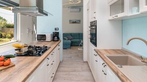 Una cocina compacta con gabinetes blancos, encimera de madera, horno integrado y ventana con vistas a un jardín.