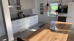 Uma cozinha moderna com armários brancos, uma mesa de jantar de madeira e luminárias pendentes.
