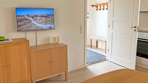 A room with a wooden cabinet, a television mounted on the wall, a wooden door, and a bench in the background.