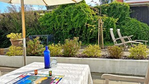 An outdoor table with a board game, a blue water bottle, and a glass. There are chairs and a white umbrella in the background.