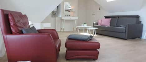 A modern loft apartment with a high ceiling, red leather sofas, a grey couch, and a small white table.