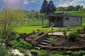 A modern building with a covered outdoor area, surrounded by a lush green landscape and a small stream. - Holiday Home in Willingen-neerdar (Willingen)