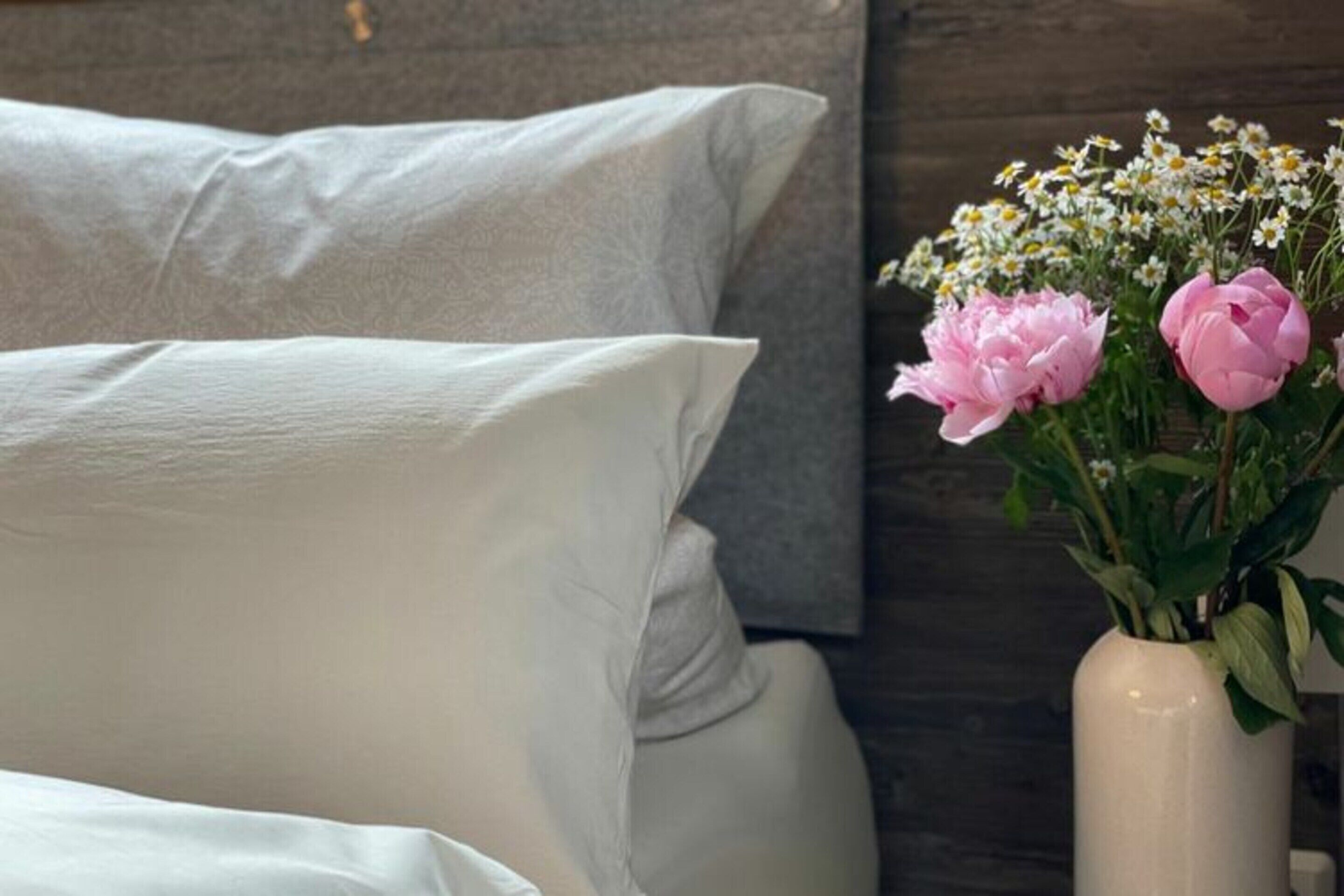 A bed with white bedding and a vase with pink flowers and baby's breath on a bedside table.
