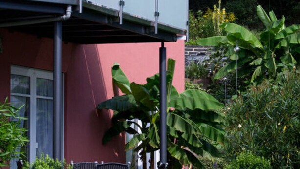 A two-story building with a balcony, surrounded by lush greenery and potted plants. - Muhlenhof - Muller Thurgau (Maring-Noviand)
