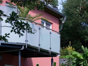 A building with a red exterior, a balcony with metal railings, and surrounding greenery.