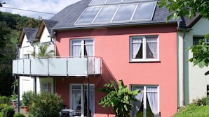 A two-story house with a red facade, a balcony with a white railing, and a sloped roof with solar panels. - Muhlenhof - Muller Thurgau (Maring-Noviand)