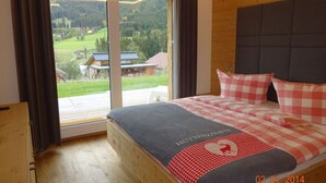 A bedroom with a large window, wooden flooring, and a bed with a checkered bedspread. - Huttenzauber 4 Comfortable Holiday Residence (Annaberg-Lungoetz)