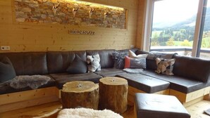 A cozy living room with a stone wall, a large window, and a leather sofa with various cushions. - Huttenzauber 4 Comfortable Holiday Residence (Annaberg-Lungoetz)