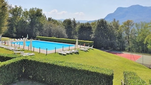 Une piscine entourée de chaises longues, bordée d’arbustes et d’arbres soigneusement entretenus, avec des montagnes en toile de fond.