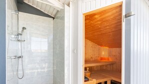 En bastu med träpanel på insidan, en duschavdelning med glasväggar och en bänk.