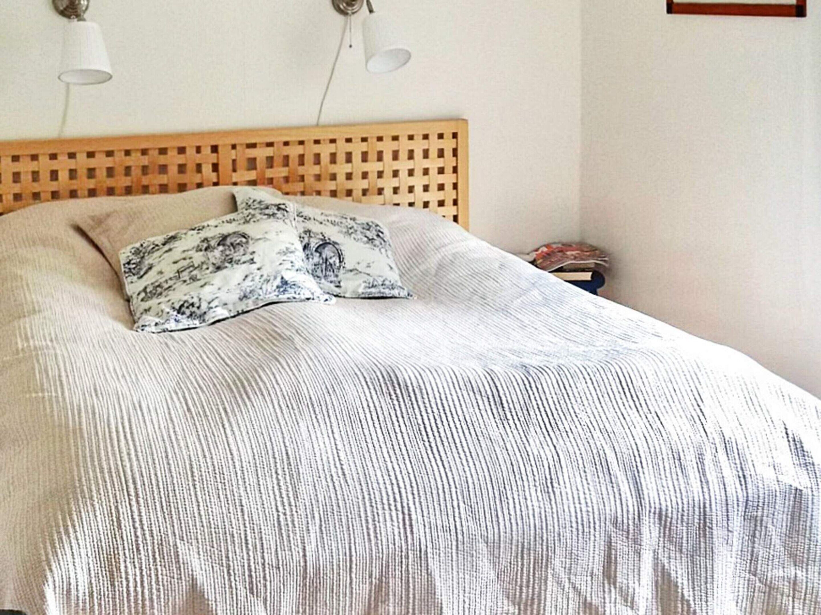 A bed with a wooden headboard, two pillows, and a white striped blanket.