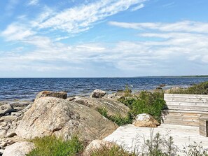A coastal scene with a wooden deck, large rocks, and the sea under a partly cloudy sky. - 4 Star Holiday Home in Sturko (Sturkö)