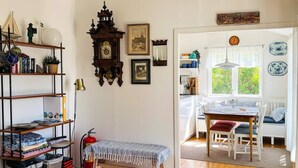 Une pièce dotée d’un plancher en bois, d’un banc, d’une bibliothèque, d’une horloge murale et d’un coin repas avec une table et des chaises.