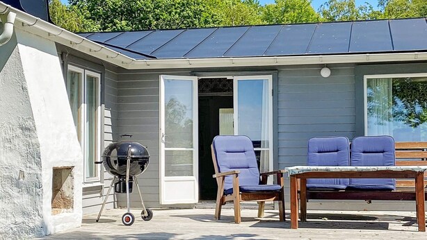 Une terrasse couverte avec un barbecue, deux chaises bleues et une table en bois.