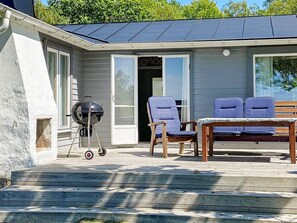 A covered patio with a grill, two blue chairs, and a wooden table. - 4 Star Holiday Home in Sturko (Sturkö)