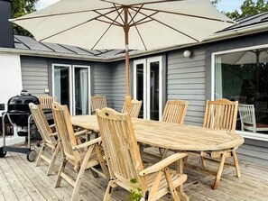 A wooden deck with a table and chairs, a grill, and an umbrella. - 4 Star Holiday Home in Sturko (Sturkö)
